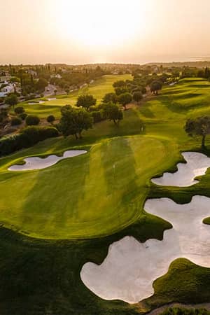 Aerial view of Aphrodite Hills Golf Course in Cyprus with green fairways, bunkers, sunset, and scenic surrounding landscapes.