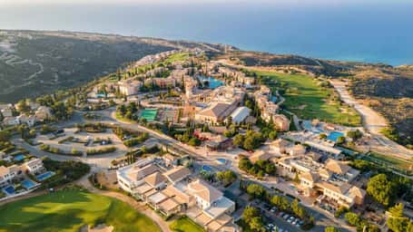 Aerial view of Aphrodite Hills Resort in Cyprus, featuring resort buildings, golf courses, and the Mediterranean Sea in the background.