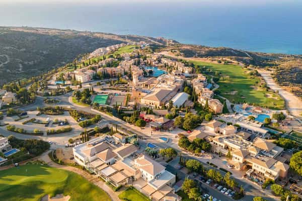 Aerial view of Aphrodite Hills Resort in Cyprus, featuring resort buildings, golf courses, and the Mediterranean Sea in the background.