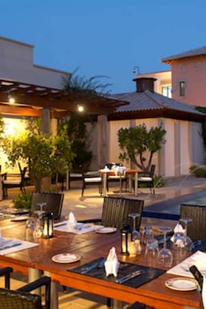 Outdoor dining area of Aphrodite Hills Resort's main restaurant in the evening, featuring elegantly set tables and a lit water feature.