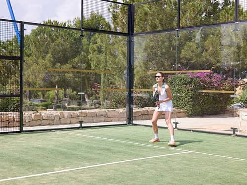 Woman playing padel tennis at Aphrodite Hills Resort, Cyprus, standing on the court with a racket and ready to receive a serve.