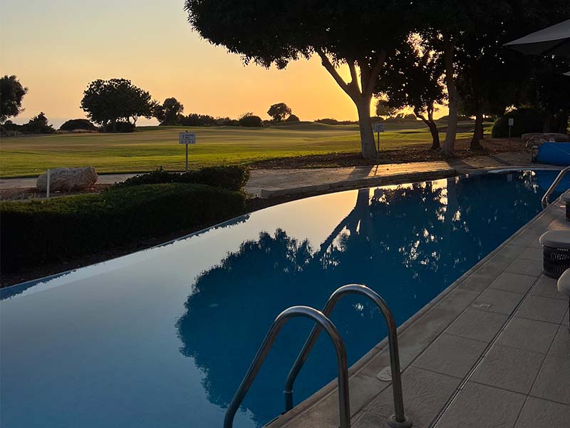Infinity pool at Aphrodite Hills Resort with sunset reflection and view of golf course.