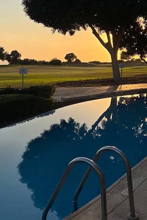 Infinity pool at Aphrodite Hills Resort with sunset reflection and view of golf course.