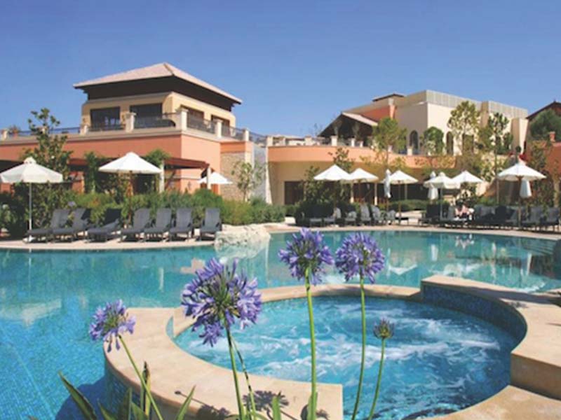 Luxurious pool area at Aphrodite Hills Resort with sun loungers, parasols, and surrounding greenery.