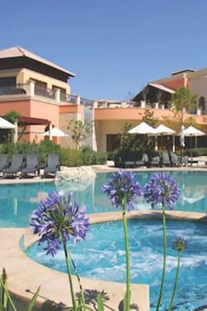 Luxurious pool area at Aphrodite Hills Resort with sun loungers, parasols, and surrounding greenery.