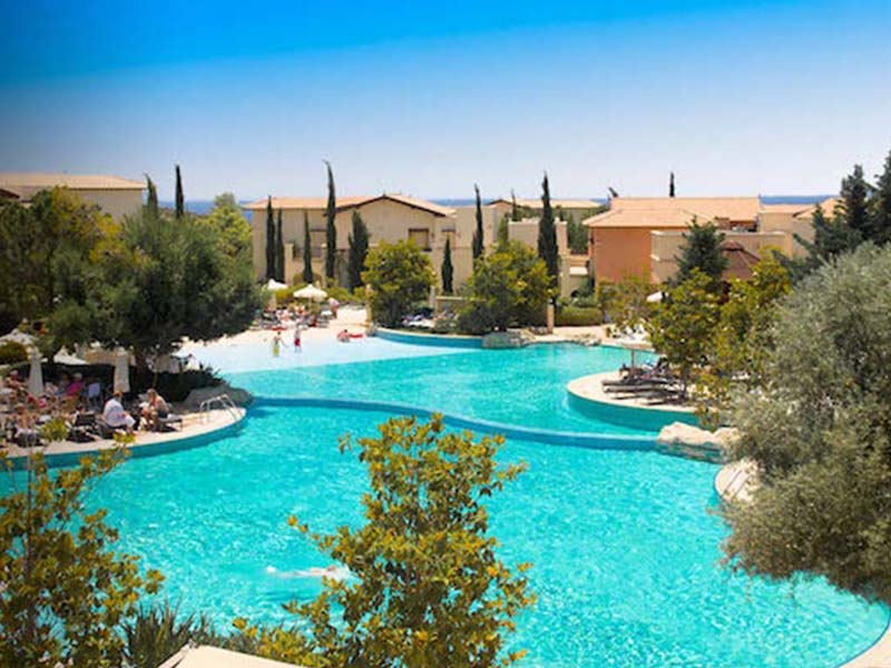 Luxurious pools at Aphrodite Hills resort surrounded by greenery and Mediterranean buildings.