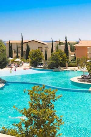 Luxurious pools at Aphrodite Hills resort surrounded by greenery and Mediterranean buildings.