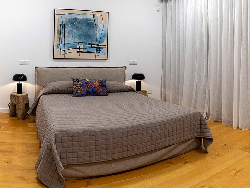 Elegant bedroom at Aphrodite Hills with a double bed, grey quilted cover, bedside tables with lamps, and an abstract wall painting.