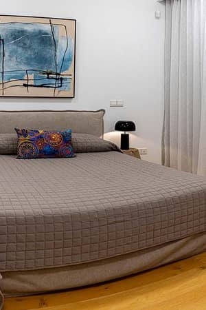 Elegant bedroom at Aphrodite Hills with a double bed, grey quilted cover, bedside tables with lamps, and an abstract wall painting.