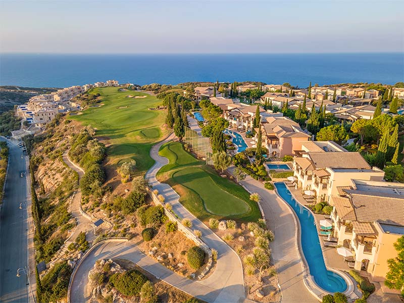 Aerial view of Aphrodite Hills in Cyprus, featuring luxury villas, a golf course, and the Mediterranean Sea in the background.