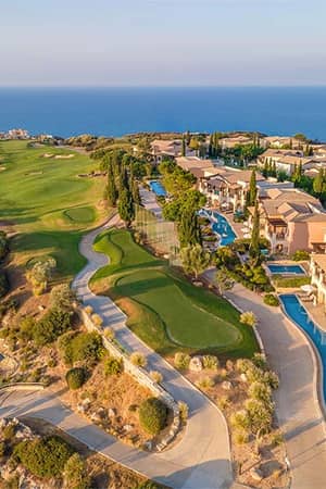 Aerial view of Aphrodite Hills in Cyprus, featuring luxury villas, a golf course, and the Mediterranean Sea in the background.