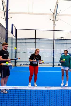Padel tennis coaching session at BD Swindon Gallery with players and a coach on a blue court.