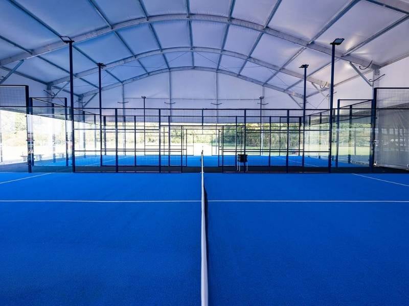 Interior of an indoor padel court at BD Swindon Gallery with a blue floor and clear glass walls under a curved white roof.