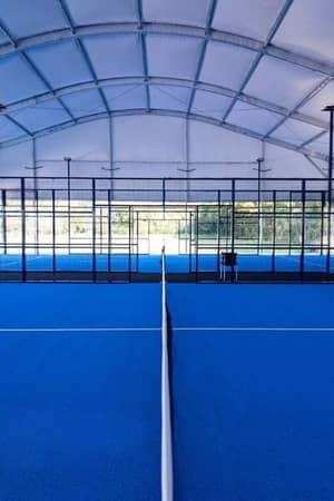 Interior of an indoor padel court at BD Swindon Gallery with a blue floor and clear glass walls under a curved white roof.