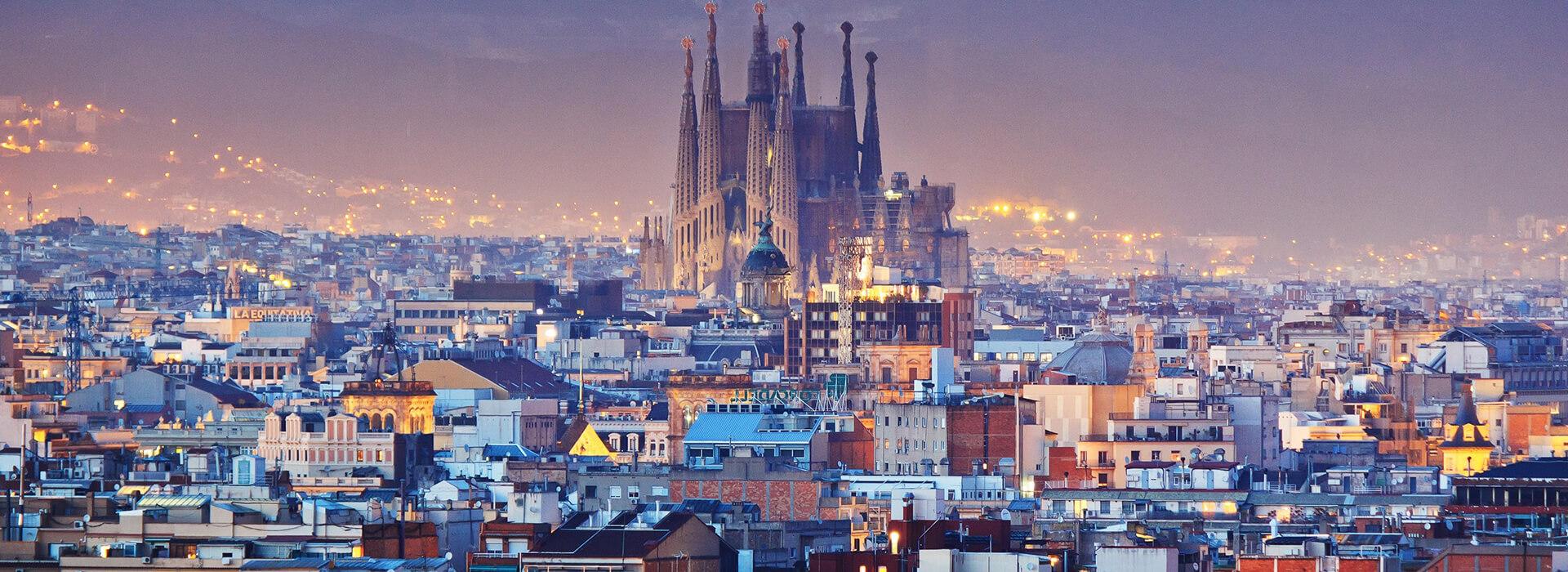 Panoramic view of Barcelona's skyline at dusk, featuring the Sagrada Familia cathedral amidst a lit-up cityscape.