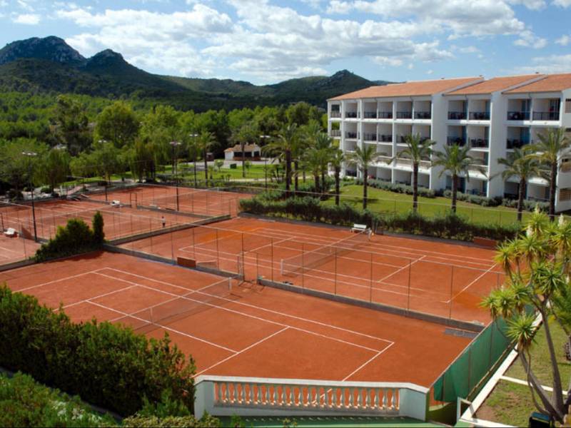Tennis courts at a beach club resort, with surrounding greenery, mountains, and a nearby hotel building.