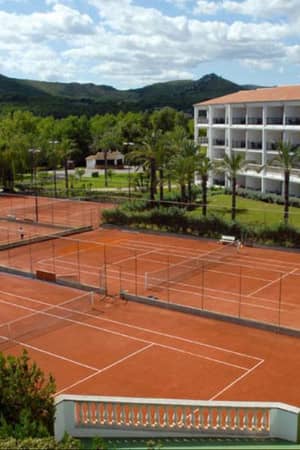 Tennis courts at a beach club resort, with surrounding greenery, mountains, and a nearby hotel building.