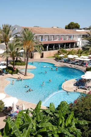 Outdoor swimming pool area at a beach club with loungers, parasols, and palm trees, set against a Mediterranean-style building.