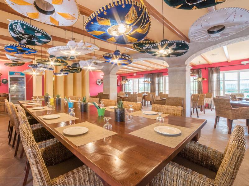 Restaurant at Beach Club Family Holiday with a long dining table, wicker chairs, and sombrero ceiling decorations.