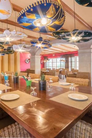 Restaurant at Beach Club Family Holiday with a long dining table, wicker chairs, and sombrero ceiling decorations.