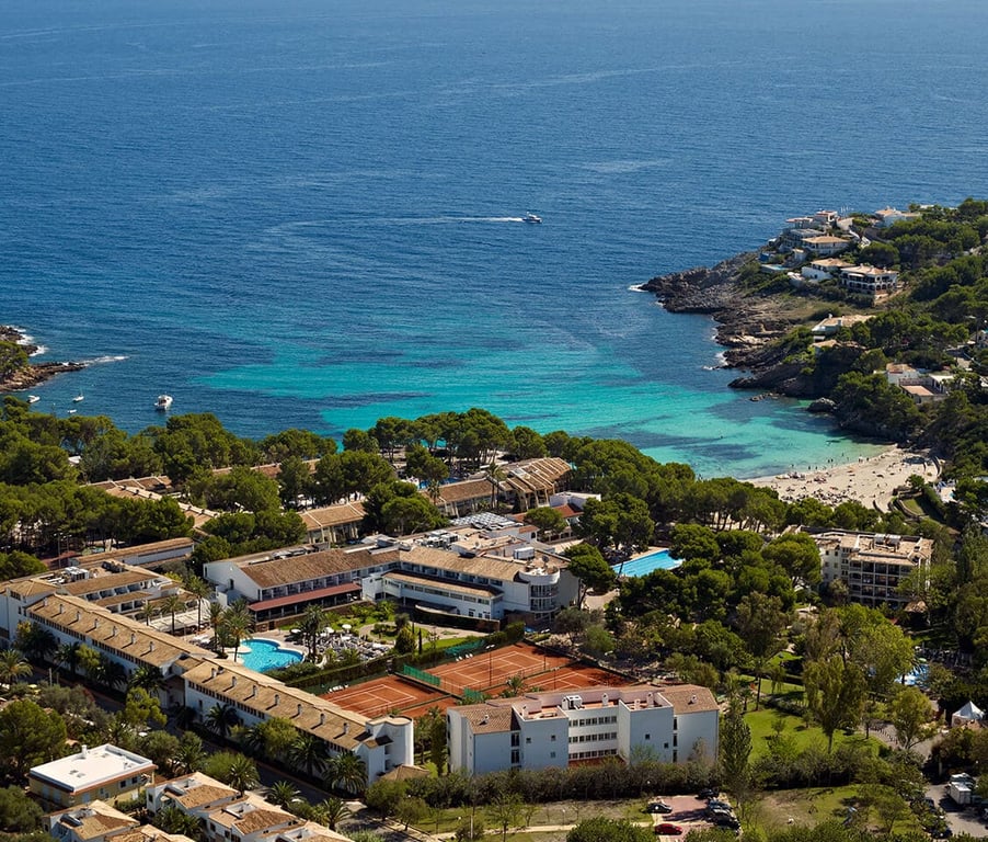 Aerial view of a beach club and resort with tennis courts and swimming pools by the turquoise sea.