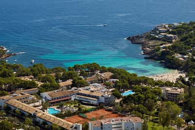 Aerial view of a beach club and resort with tennis courts and swimming pools by the turquoise sea.