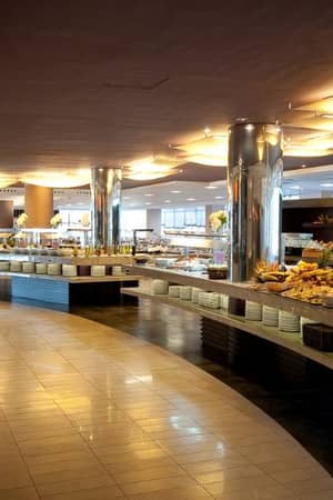 Luxurious beach club buffet with curved counters and an assortment of fruits, pastries, and gourmet dishes under ambient lighting.