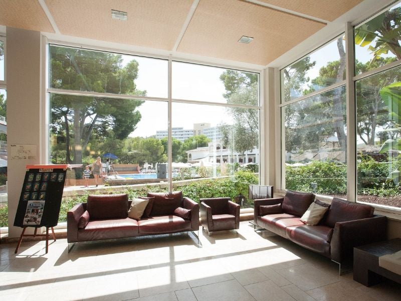 Beach club lobby with leather sofas and large windows overlooking an outdoor pool area and greenery.