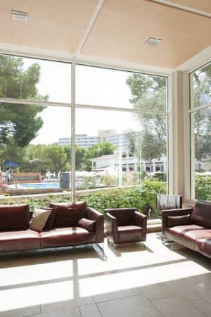 Beach club lobby with leather sofas and large windows overlooking an outdoor pool area and greenery.