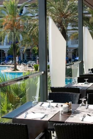 Outdoor dining area at a beach club restaurant with tables overlooking a pool and palm trees.