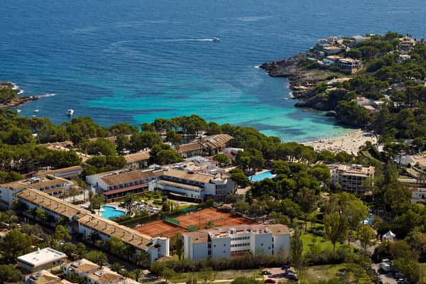Aerial view of a beach club with resort facilities, tennis courts, pool, and coastline with turquoise waters and sandy beaches.