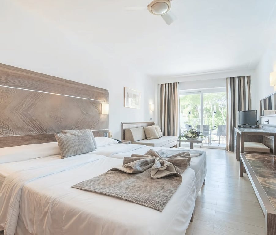 Modern beach club standard room with two beds, desk with TV, and balcony overlooking greenery.