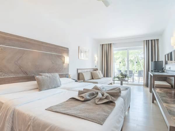 Modern beach club standard room with two beds, desk with TV, and balcony overlooking greenery.