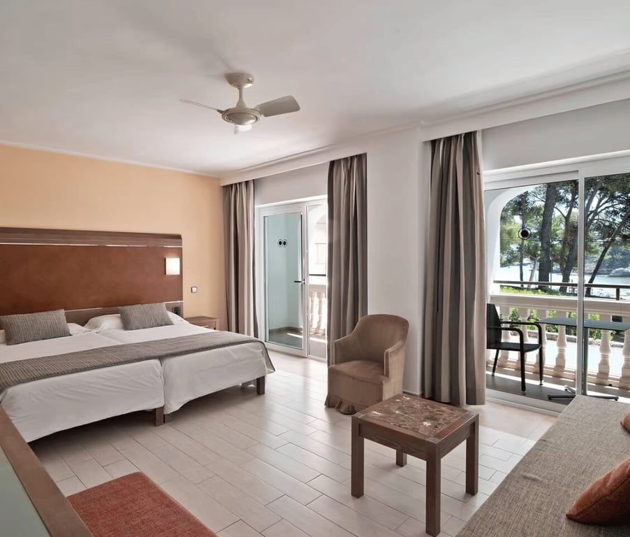 Beach club standard room with two single beds, a balcony showing a sea view, an armchair, and neutral decor.