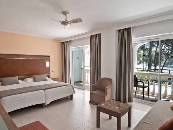 Beach club standard room with two single beds, a balcony showing a sea view, an armchair, and neutral decor.