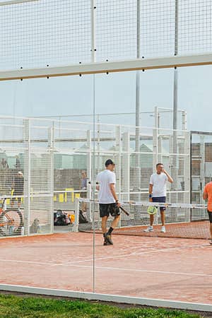 Players playing doubles padel tennis on an outdoor glass-walled court in Brighton.
