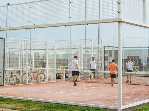 Players playing doubles padel tennis on an outdoor glass-walled court in Brighton.