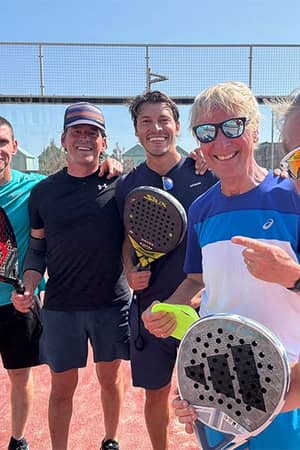 Five people standing on a red padel court, each holding a padel racket, on a sunny day in Brighton.