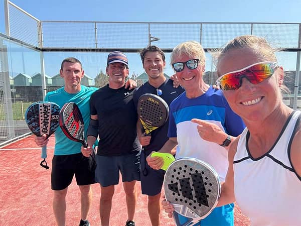 Five people standing on a red padel court, each holding a padel racket, on a sunny day in Brighton.