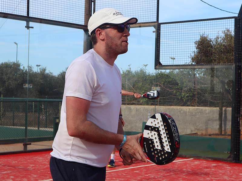 Man wearing a white t-shirt and cap, holding a padel racquet on a court in Brighton, ready to play.