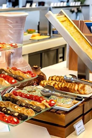 Buffet arrangement at Capo Bay Gallery showcasing assorted pastries, sandwiches, and breads on glass stands with condiments in the background.