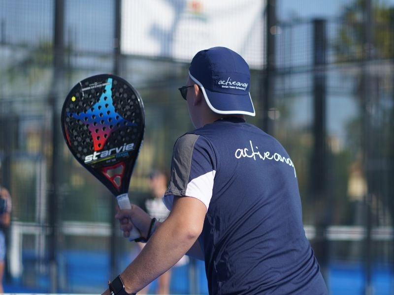 Padel coach holding a StarVie racket on an outdoor court with a blue activewear uniform.