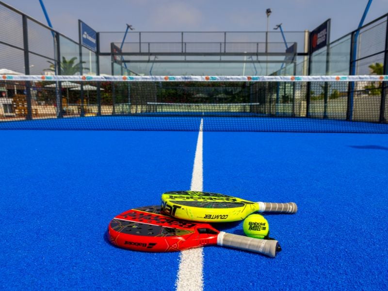 Vibrant blue padel court at Capo Bay Gallery with two rackets placed on the surface near the net.
