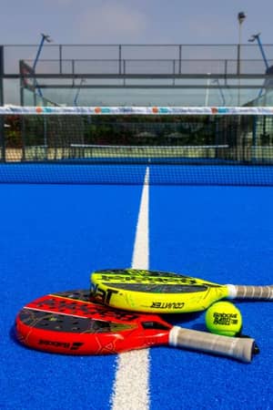 Vibrant blue padel court at Capo Bay Gallery with two rackets placed on the surface near the net.