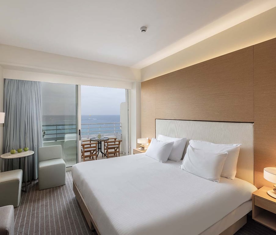 Luxurious hotel room at Capo Bay Hotel with a double bed, modern decor, and a balcony offering a sea view.