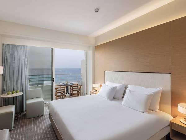 Luxurious hotel room at Capo Bay Hotel with a double bed, modern decor, and a balcony offering a sea view.