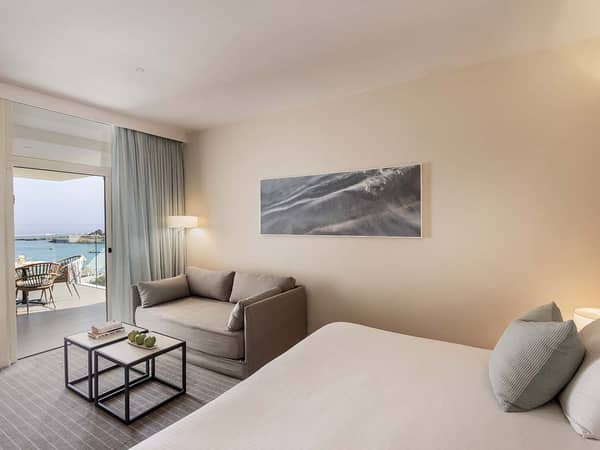 Hotel room with modern decor, comfortable bed, grey sofa, and a balcony with sea views.