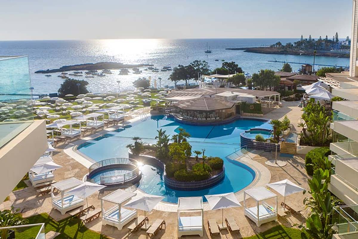 Overhead view of Capo Bay Hotel's pool area with sun loungers, umbrellas, and the Mediterranean Sea in Protaras, Cyprus in the background.