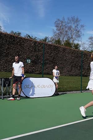 Jamie Murray on a tennis court with junior students at Churcher's School, during a training session with an ACE ACADEMY banner in the background.