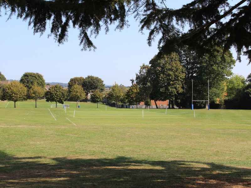 Churcher's School outdoor grass courts on a sunny day, with rugby posts and sports field markings surrounded by trees.